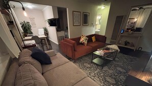 Ein Wohnzimmer mit einer Couch, einem Couchtisch und einem Teppich. Es gibt einen Essbereich mit Stühlen und einem Tisch.