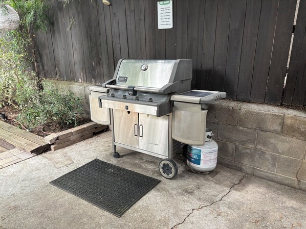 Un barbecue au gaz portatif, doté d’un meuble latéral et d’une bouteille de gaz.