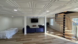 A spacious living room with a wooden floor, a blue sofa, a flat-screen TV, and a spiral staircase.