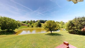 A serene outdoor setting with a pond, trees, and a wooden deck.