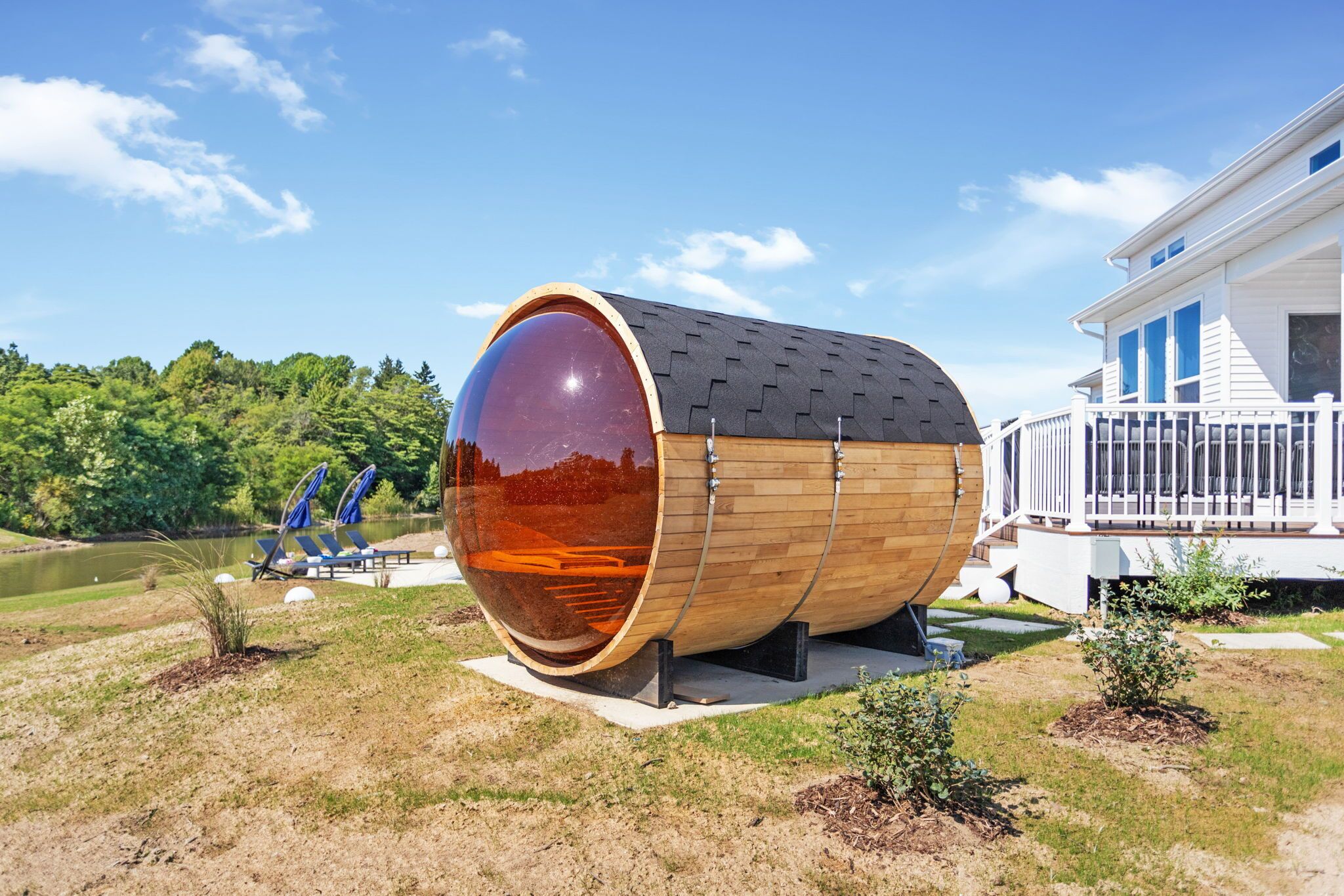 Una gran estructura de bigues de fusta amb una superfície reflectant, situada en una zona enjarditada amb una casa al fons.