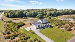 Une maison à deux étages avec un garage, entourée d’une pelouse bien entretenue et d’un étang.