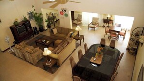 A spacious living room with a large black glass table, multiple sofas, and a television set.