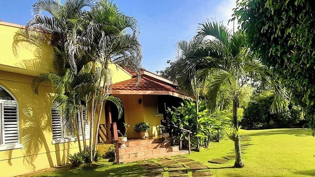 A yellow building with a red roof, surrounded by palm trees and a well-maintained lawn.