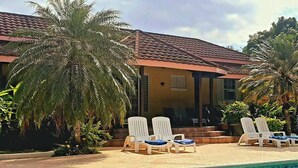 A poolside area with lounge chairs, palm trees, and a building with a tiled roof.