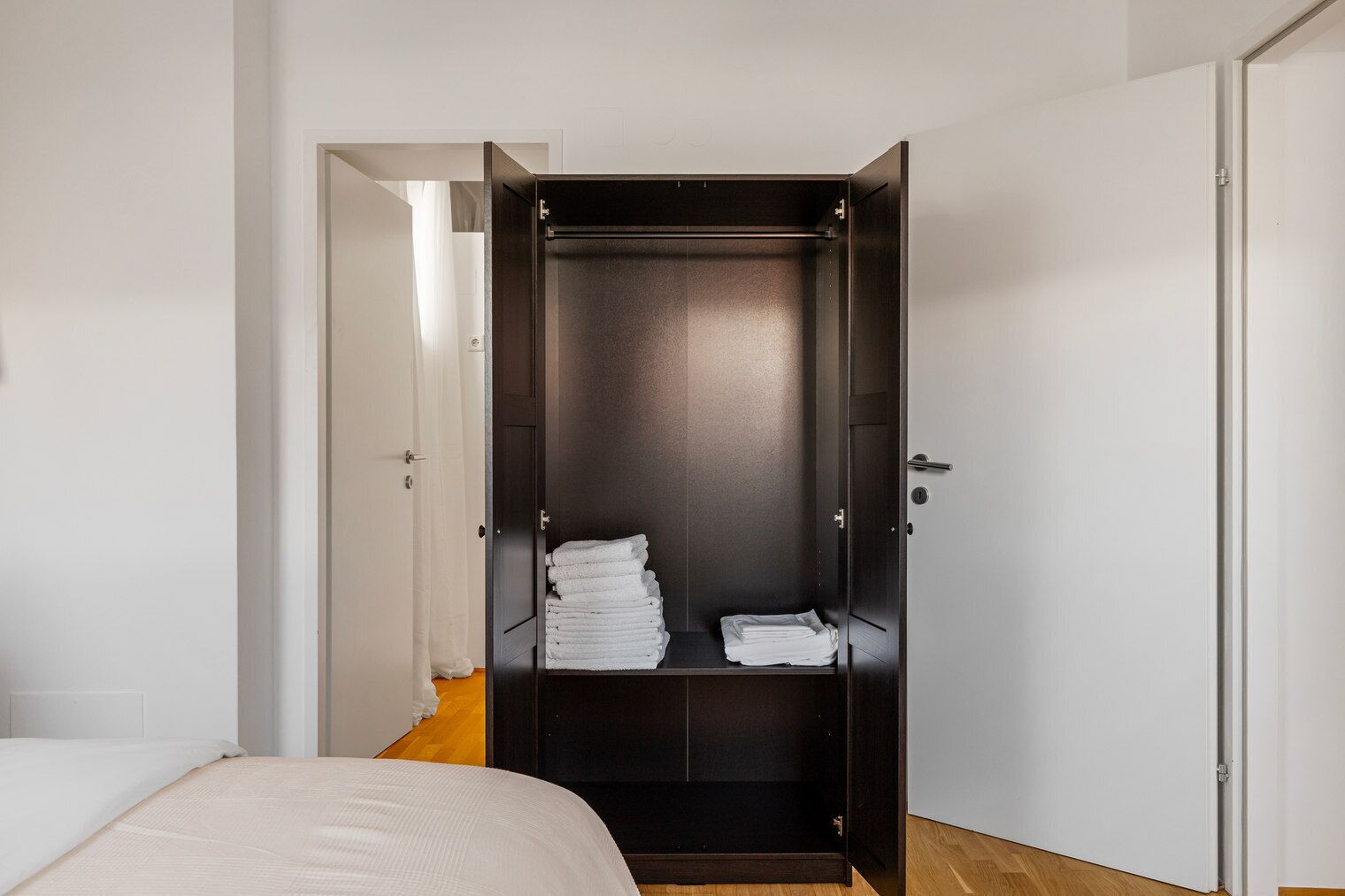A bedroom with a bed, a dark-colored wardrobe with a mirror, and a door leading to another room.