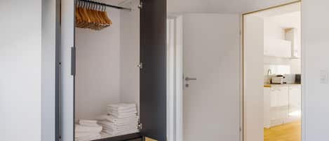 A modern bedroom with a wardrobe, a neatly made bed, and a view into the kitchen.