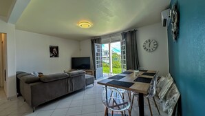 A living room with a sofa, TV, and a dining area with a table and chairs. - Wave & Chill Apartment with garden 2 steps from the sea (Sainte-Luce)