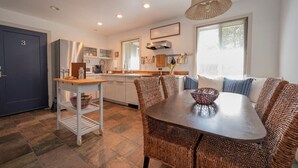 A modern kitchen with a dining area, featuring a dark blue door, a wooden table, wicker chairs, and a hanging light fixture. - King + 2 Queen Beds | 3 Smart TV`s | *WALK to LU* (Lynchburg)