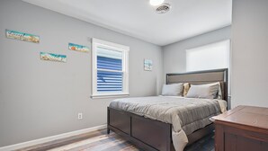 Un dormitorio con cama, ventana con persianas y una mesita.