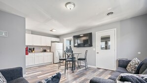 Una sala de estar moderna con un sofá gris, un comedor con mesa y sillas, y una cocina al fondo.