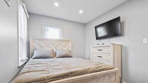 A bedroom with a bed, a TV, a dresser, and a window.