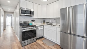 A modern kitchen with white cabinets, stainless steel appliances, and a wooden floor.
