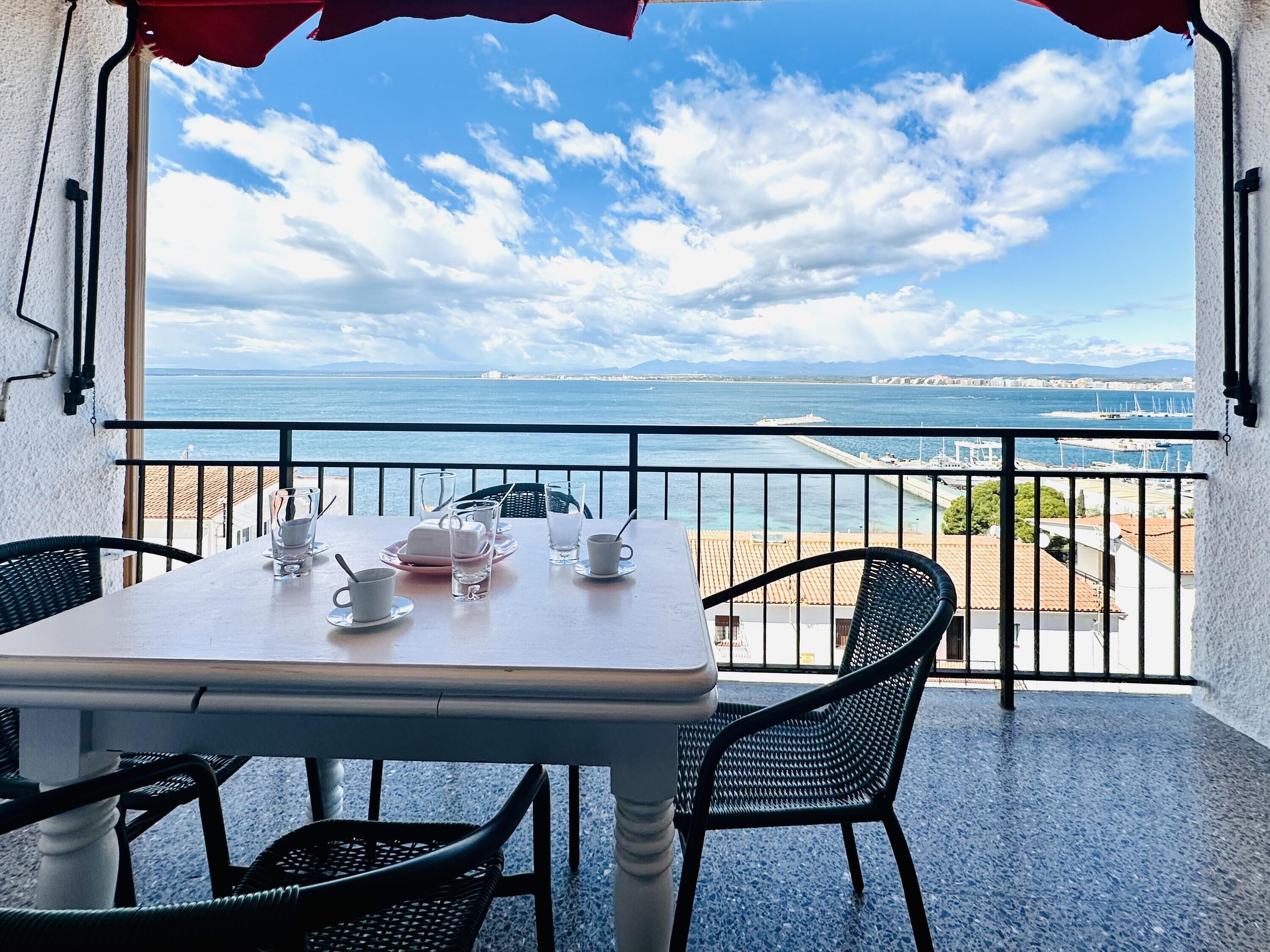 A balcony with a table set for two, overlooking a coastal view.
