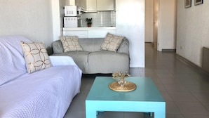 A modern living room with a sofa, a coffee table, and a kitchen in the background. - Charming Apartment Near the Beach and Town Centre (Roses)