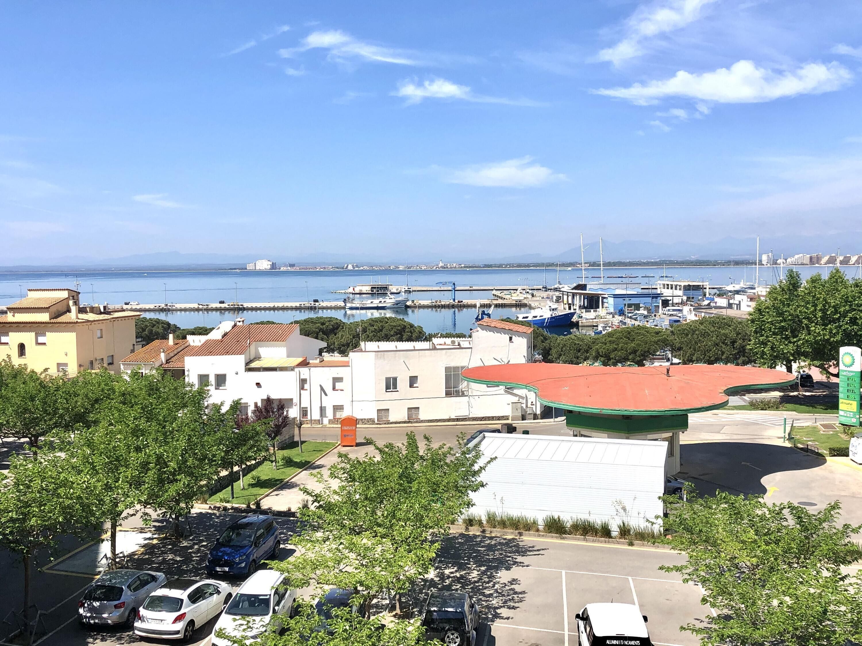 A coastal town with buildings, a marina, and parked cars.