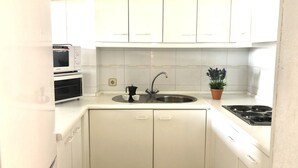 A compact kitchen with white cabinets, a stainless steel sink, a stove, and a microwave. - Charming Apartment Near the Beach and Town Centre (Roses)