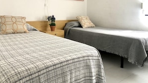 A bedroom with two beds, a nightstand with a plant, and a wall-mounted lamp. - Charming Apartment Near the Beach and Town Centre (Roses)