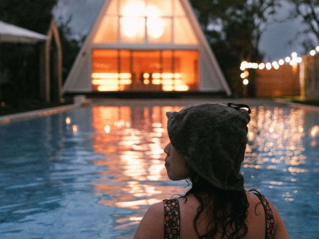 Une personne se tient près d’un bassin dont la surface est réfléchissante, avec un bâtiment en arrière-plan.