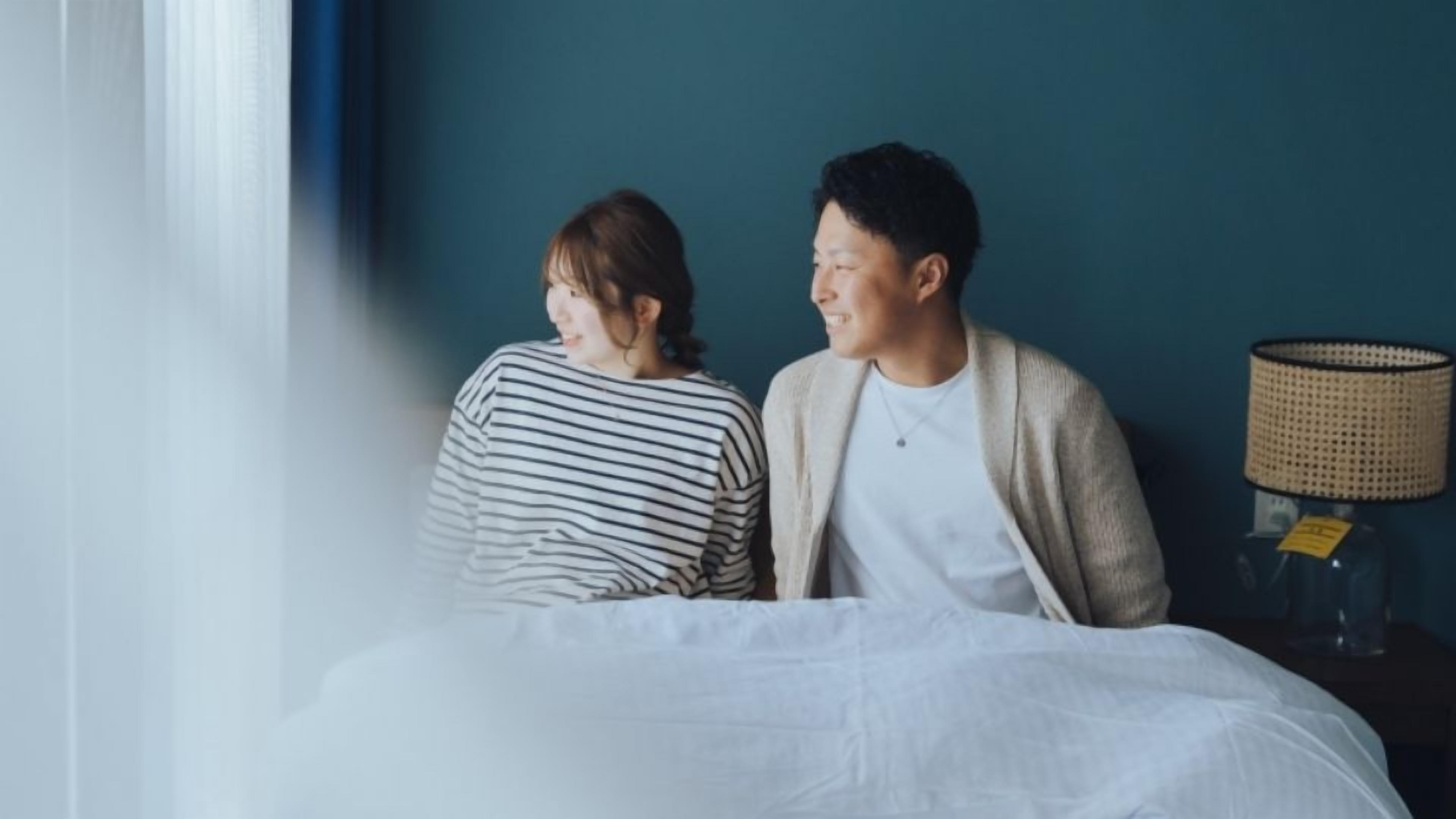 A room with a bed, a nightstand with a lamp, and a window with curtains.