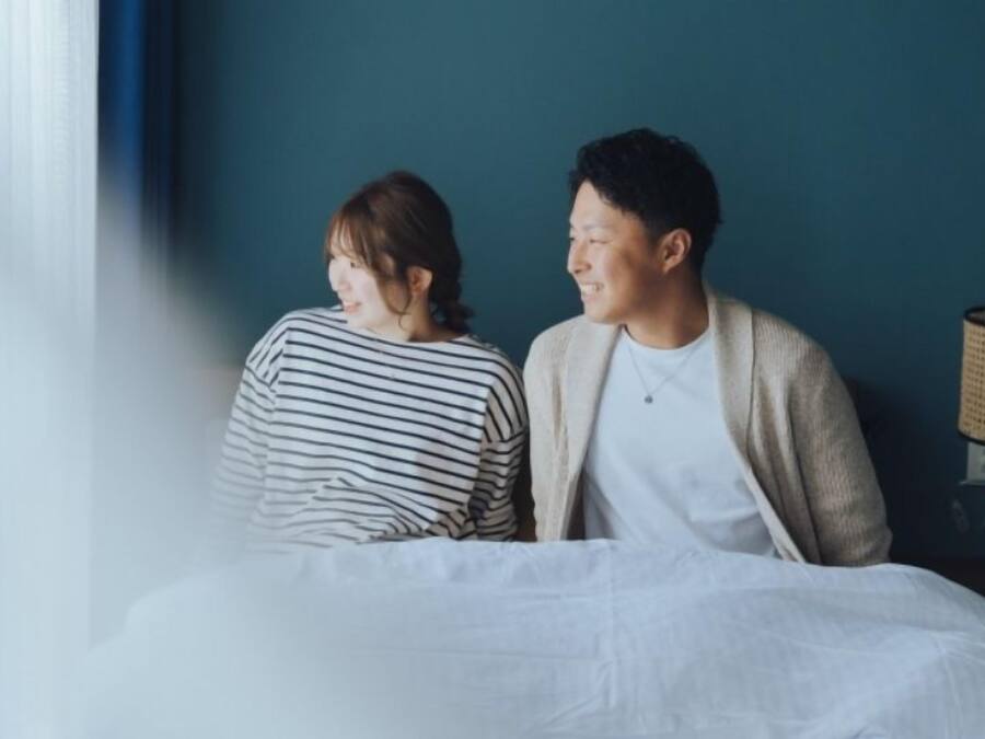 A room with a bed, a nightstand with a lamp, and a window with curtains.