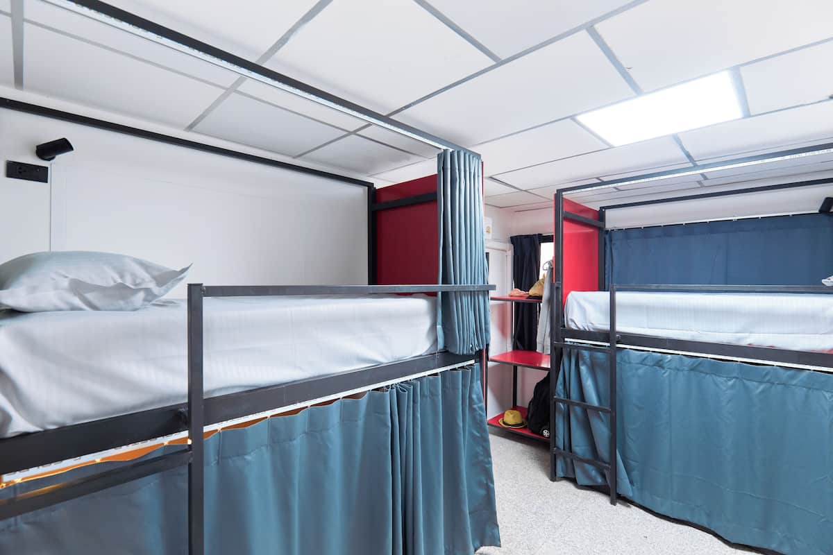 A dormitory room with bunk beds, a red wall, and a shelf with personal items.
