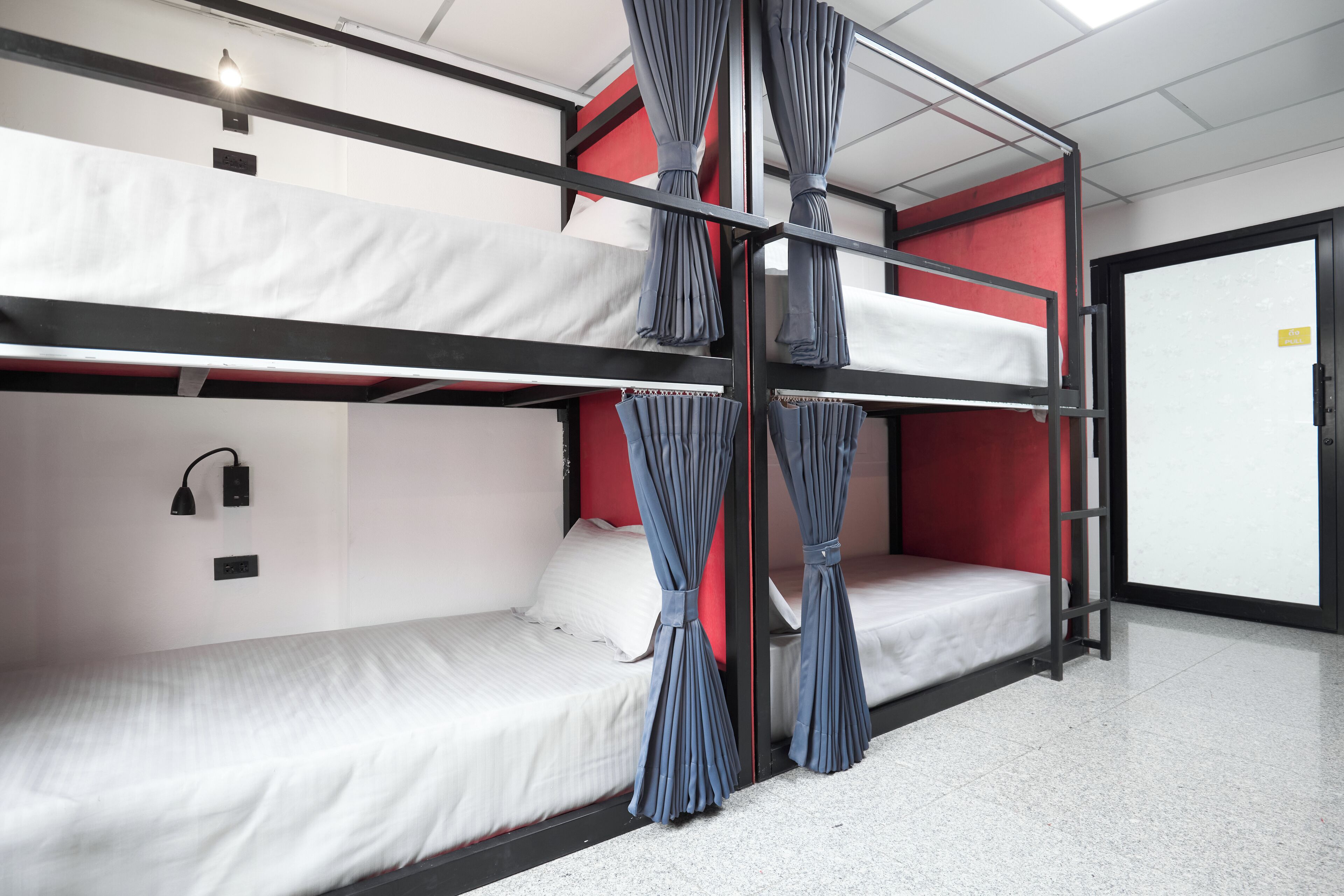 A bunk bed room with a red accent wall, a door with a sign, and a light fixture.
