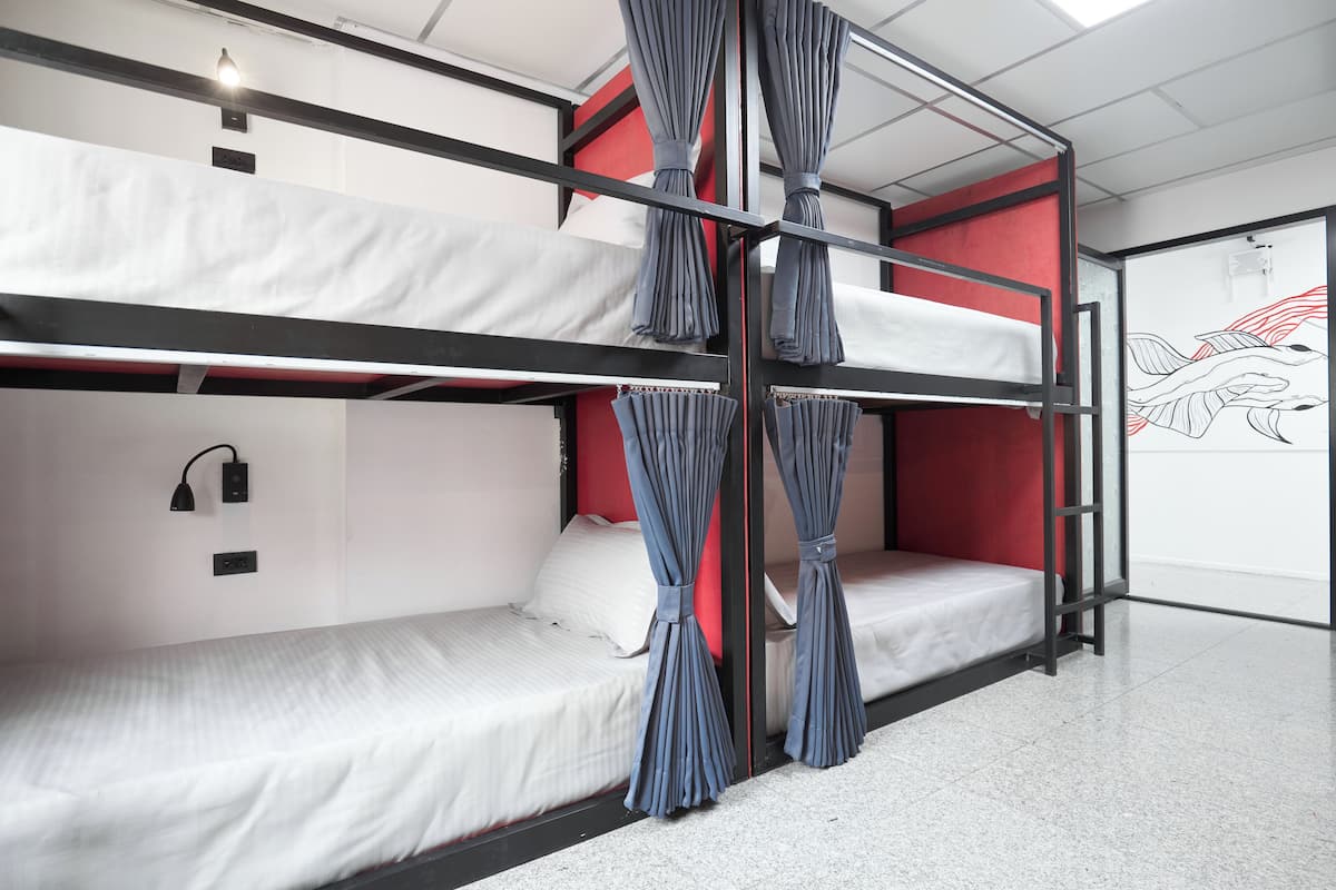 A bunk bed room with a red wall, white bedding, and curtains.