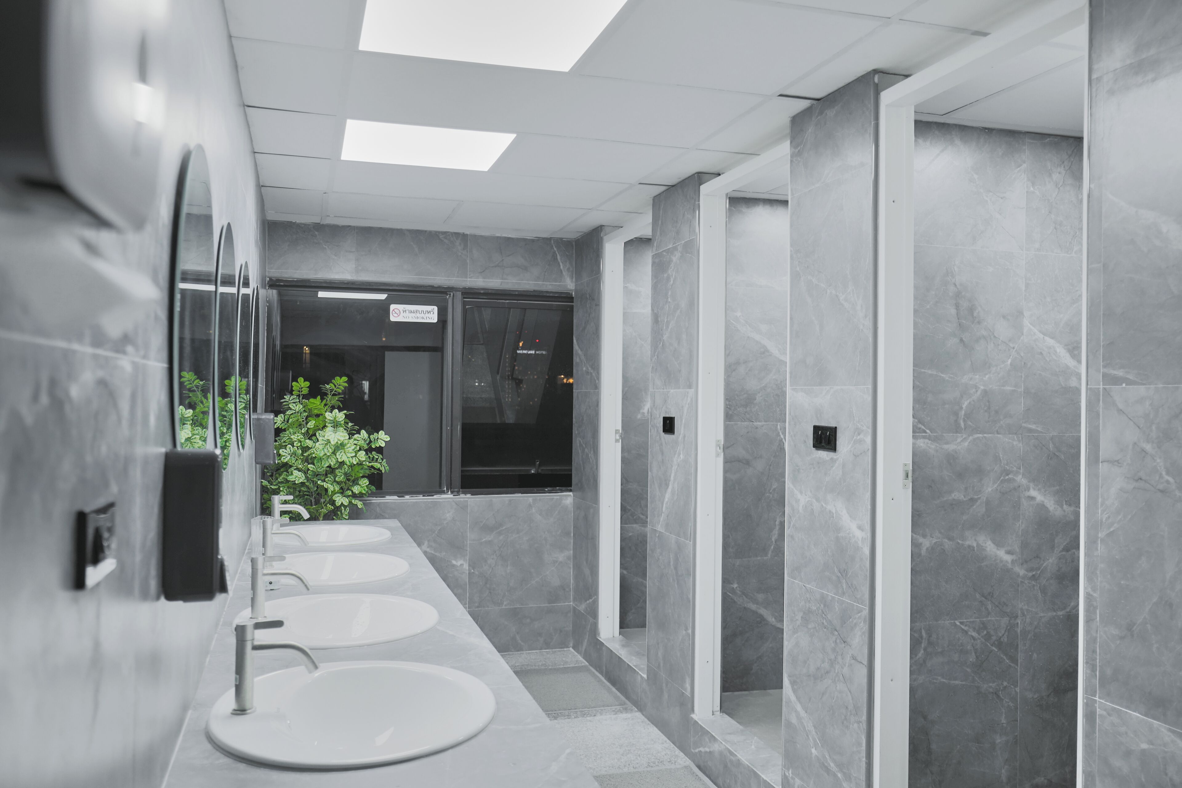 Un baño moderno con tres lavamanos, un espejo y una planta en maceta.
