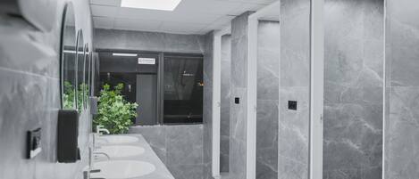 Un baño moderno con tres lavamanos, un espejo y una planta en maceta.