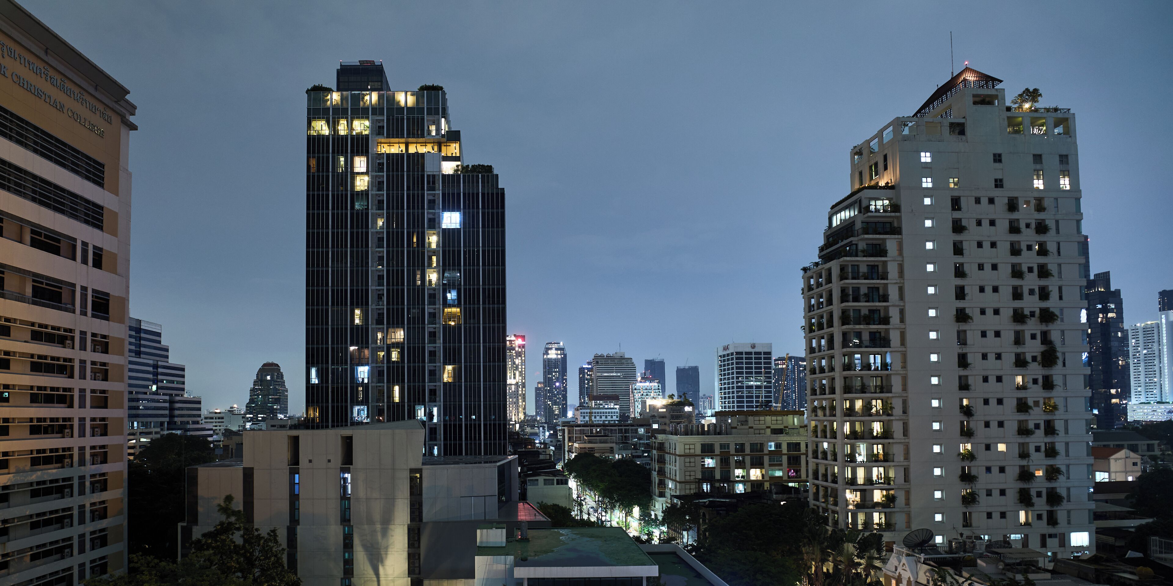 Un paysage urbain avec de hauts immeubles, dont un bâtiment remarquable avec des fenêtres illuminées et un jardin sur le toit.