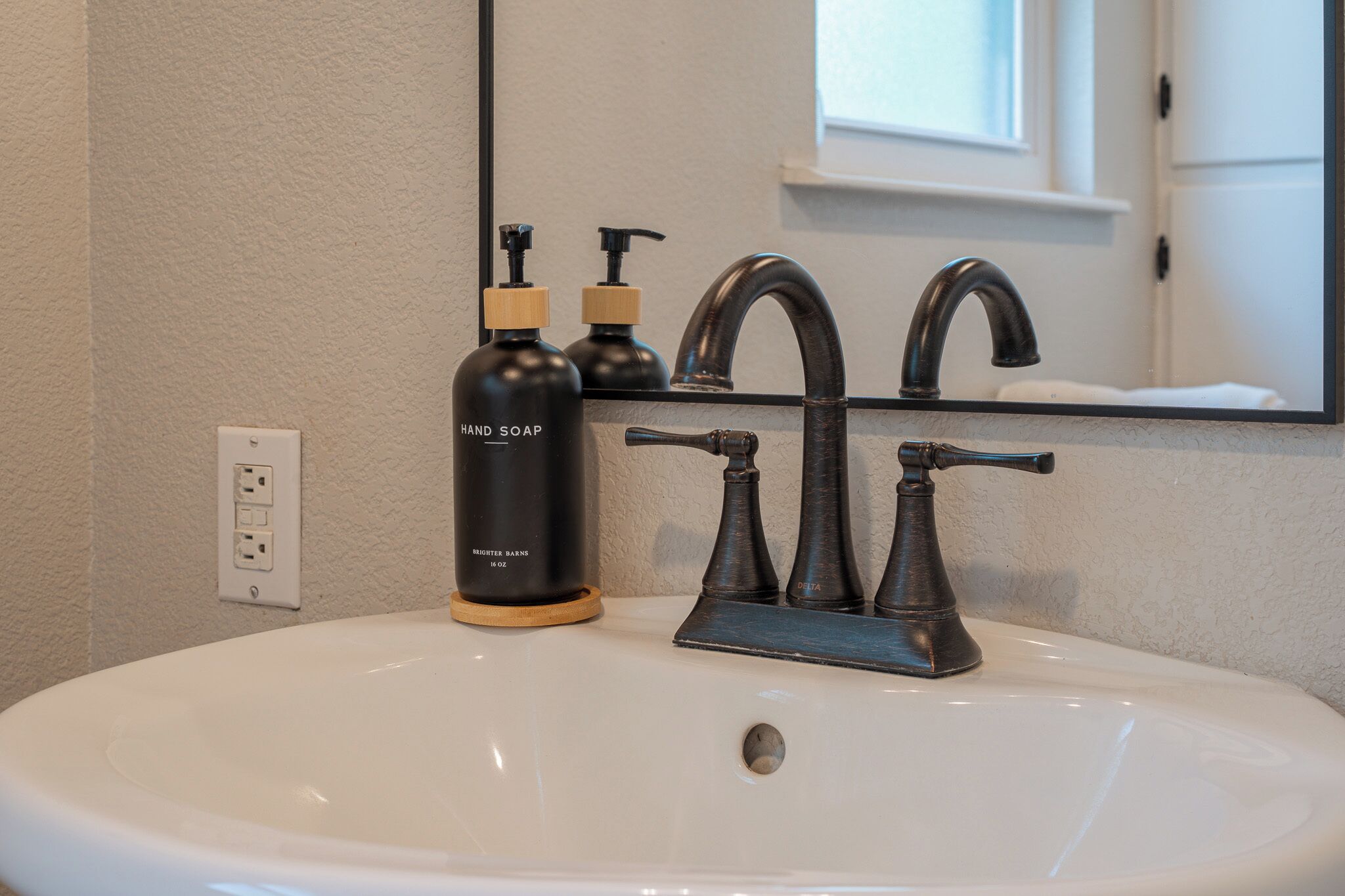 A bathroom with a white sink, a mirror, a black faucet, and two black soap dispensers.