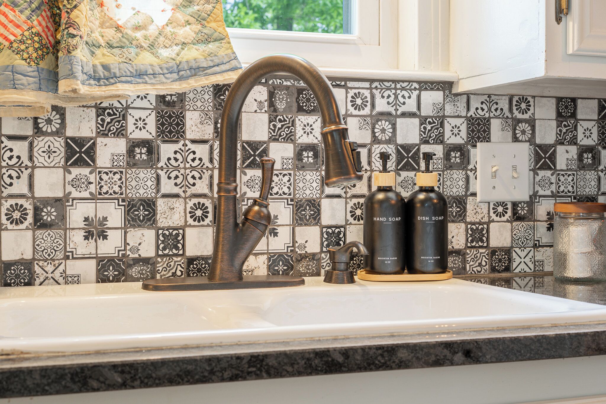 A kitchen with a decorative backsplash, a sink, and two soap dispensers.