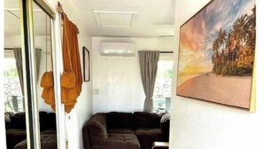 Un salon moderne avec un canapé d’angle brun foncé, une porte vitrée donnant sur l’extérieur et un tableau représentant un coucher de soleil accroché au mur.