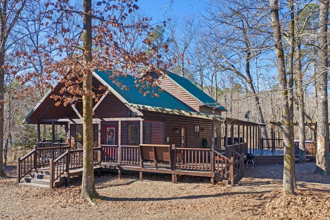 A rustic cabin with a green roof, wooden deck, and a porch with benches.