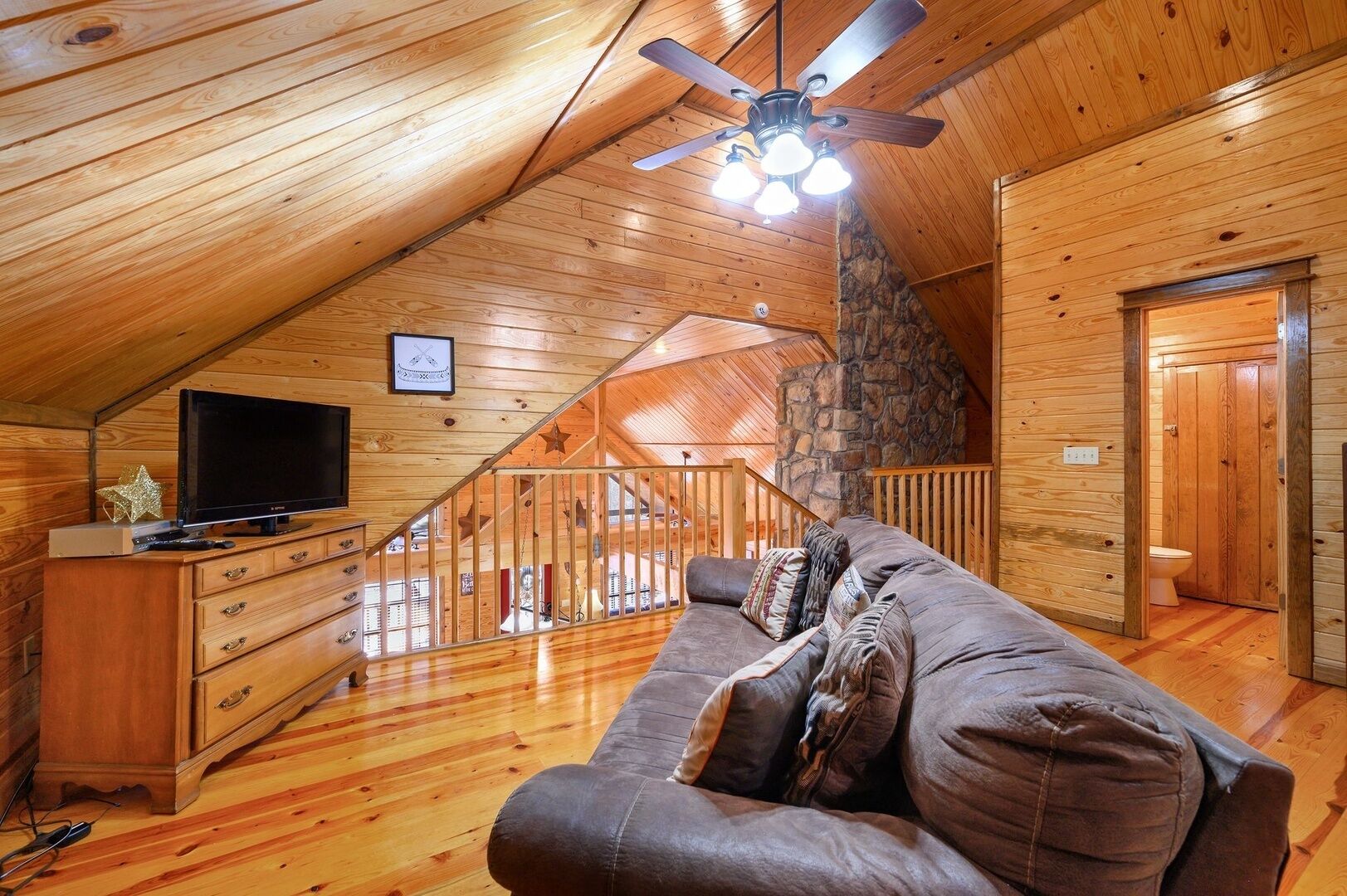 Ein gemütliches Blockhaus-Interieur mit Holzbalkendecke, Kamin aus Stein, Holztreppe, Ledersofa und Fernseher auf einem Holzschrank.