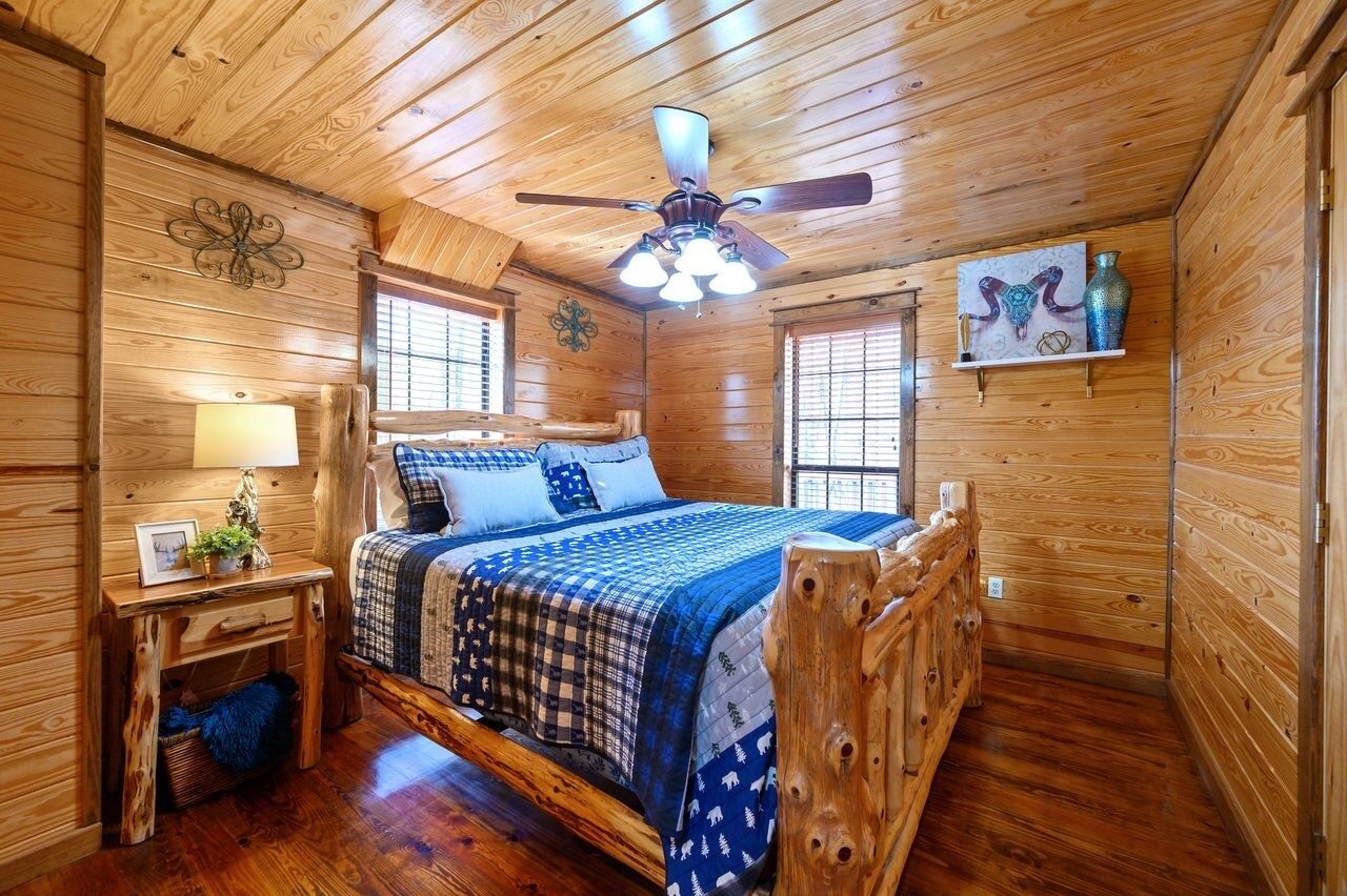 A wooden cabin bedroom with a bed, a nightstand, a lamp, and a ceiling fan.