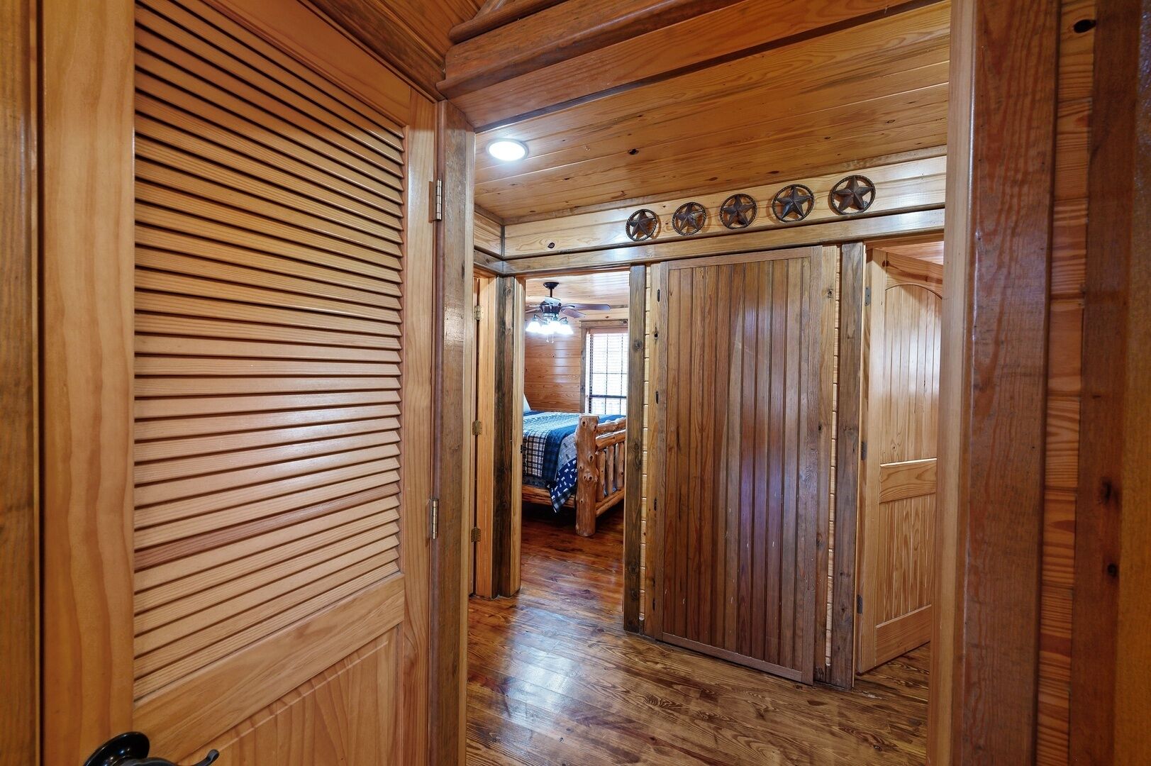 A wooden hallway leading to a bedroom with a bed and a window.
