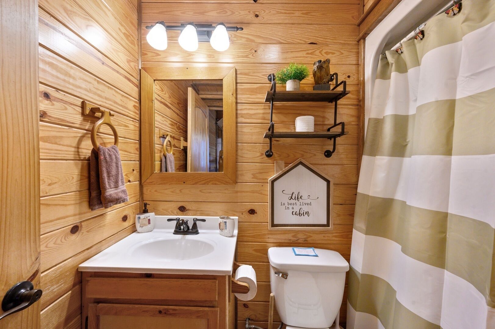 A cabin-style bathroom with a wooden interior, a sink, a toilet, a mirror, and a shower curtain.