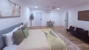 A spacious living room with a large bed, a dining area, and a dark-colored sofa.