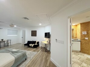 A modern bedroom with a bed, a desk, a black sofa, and a TV.