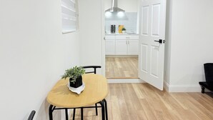 A narrow hallway leading to a kitchen with white cabinets, a stainless steel range hood, and a dining area with a wooden table and chairs.