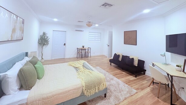 A modern, well-lit bedroom with a bed, a sofa, a desk, and a TV.