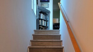 Eine Holztreppe mit Handlauf, die zu einem Raum führt, in dem Bücherregal und gerahmte Bilder an der Wand zu sehen sind.