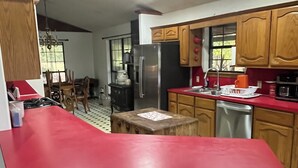 Una cucina con mobili in legno, un piano di lavoro rosso, un frigorifero in acciaio inossidabile e un'area pranzo con un lampadario.