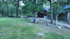 Un rustico chalet con un vialetto sterrato, circondato da alberi e da un prato.