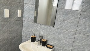 A bathroom with a white pedestal sink, a mirror, and a trash bin. - Feiloakimisi (Nuku'alofa)