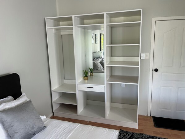 A bedroom with a large white wardrobe, a bed with grey and white bedding, and a white door.