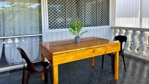 A wooden table with a potted plant on a balcony with a metal grill window, a chair, and a railing. - Feiloakimisi (Nuku'alofa)