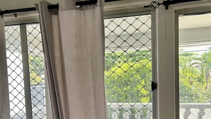 A room with a wooden table, a window with a metal screen, and a view of greenery outside. - Feiloakimisi (Nuku'alofa)